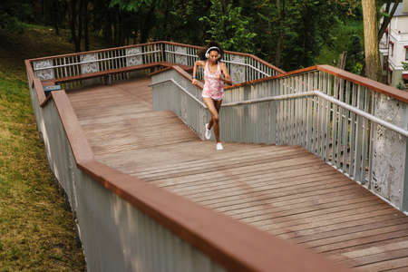 Young black woman listening music with headphones while running up stairs outdoorsの写真素材