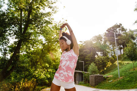 Young black woman in headphones doing exercise while working out outdoors