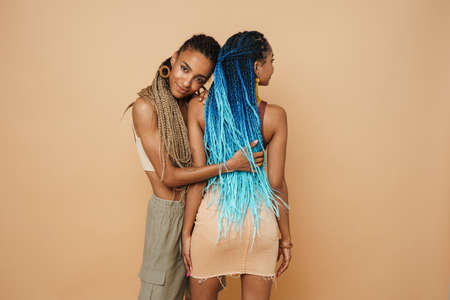 Young black two women hugging while posing on camera isolated over beige backgroundの写真素材