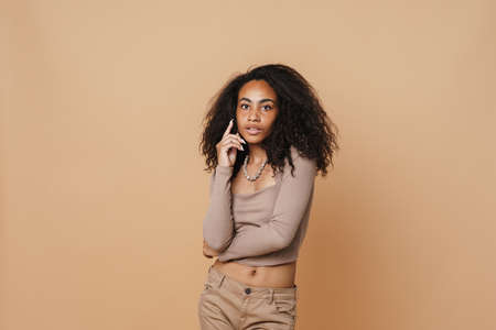 Young black woman with necklace posing and looking at camera isolated over beige backgroundの写真素材