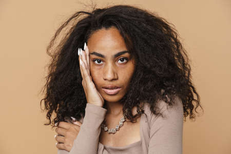 Young black woman with necklace posing and looking at camera isolated over beige background