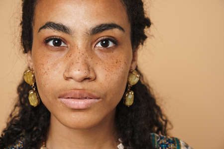 Young black woman wearing earrings looking at camera isolated over beige backgroundの写真素材