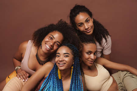 Young black four women smiling while posing together on camera isolated over brown backgroundの写真素材