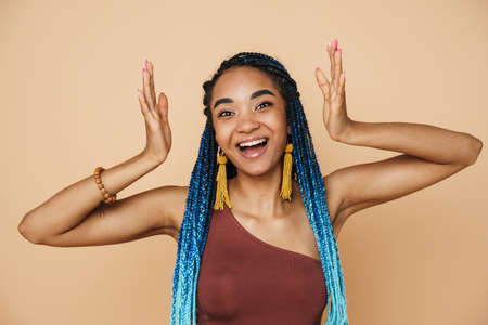 Young black woman with blue afro pigtails laughing and gesturing at camera isolated over beige backgroundの写真素材