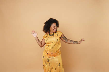Young black woman with tattoo laughing while dancing on camera isolated over beige background