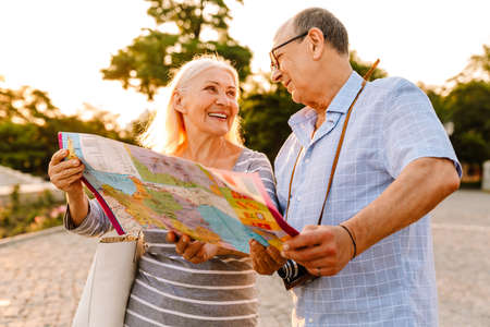 White senior couple smiling and examining map while walking in summer parkの写真素材