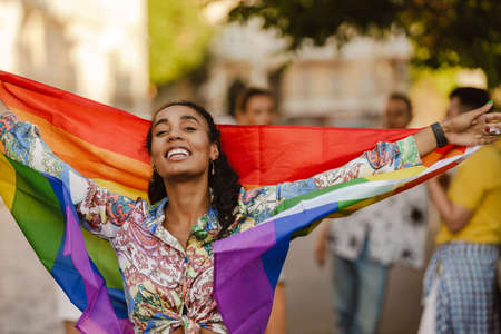 Black woman smiling and holding rainbow flag during pride parade at city street
