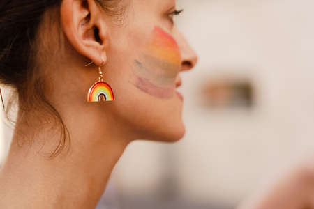White woman with rainbow sign on her cheek smiling during pride parade at city streetの写真素材