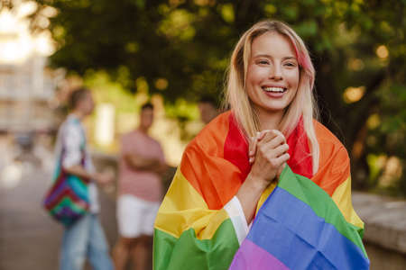 White woman laughing and holding rainbow flag during pride parade at city street