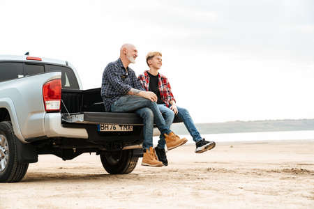 Smiling father and his son sitting in a car trunk on a back at the beach