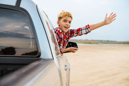 Teenage boy looking out of a car window driving on the beach