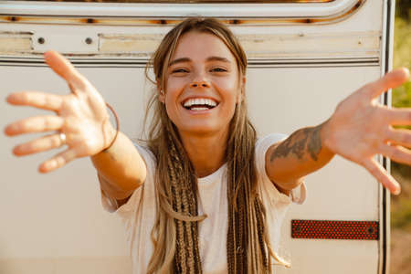 White young woman smiling and reaching her hands at camera by trailer outdoors
