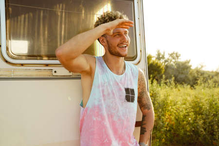 Ginger young man smiling and looking aside while leaning on trailer outdoorsの写真素材