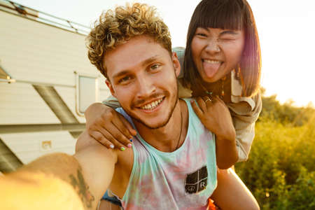 Multiracial couple taking selfie while piggybacking by trailer outdoorsの写真素材