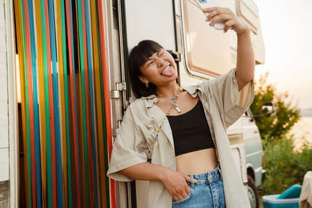 Asian young woman taking selfie on cellphone by trailer outdoors