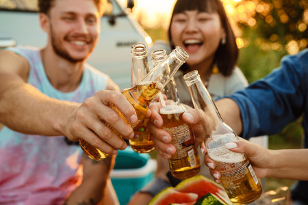 Multiracial friends drinking bear and talking during picnic by trailer outdoors