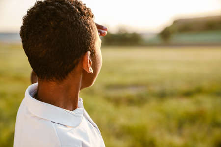 Black boy wearing white shirt looking at sunset while standing on summer fieldの写真素材