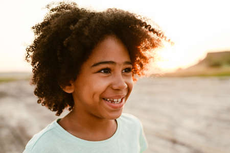 Black curly boy wearing t-shirt smiling and looking aside outdoorsの写真素材