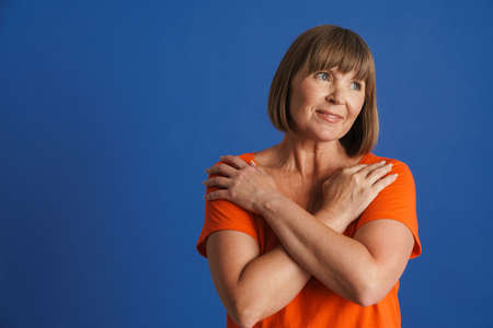 Senior woman wearing t-shirt posing with arms crossed on her chest isolated over blue wall