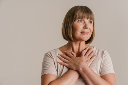 Senior woman holding crossed hands on her chest and looking aside isolated over white wall