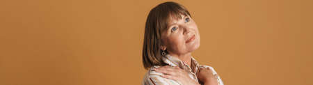 Senior woman wearing shirt posing with arms crossed on her chest isolated over beige wall