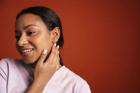 Young black woman wearing t-shirt smiling and looking aside isolated over red wall