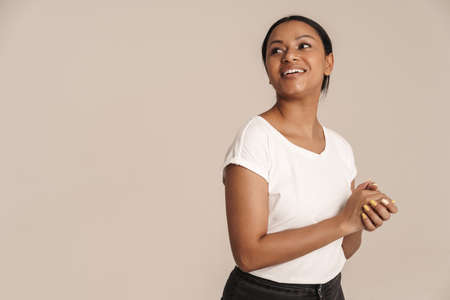 Young black woman wearing t-shirt smiling and looking aside isolated over white wall