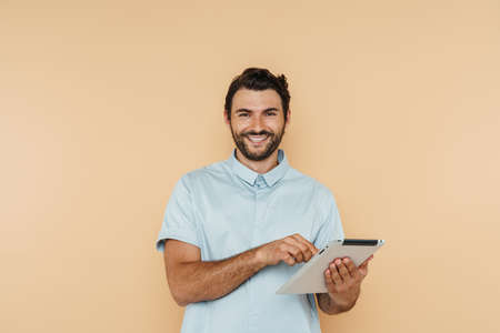 White bristle man smiling and using tablet computer isolated over beige background