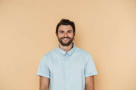 Young white man wearing shirt smiling and looking at camera isolated over beige backgroundの写真素材