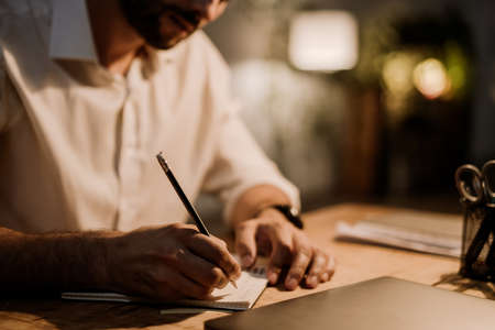 White bearded man writing down notes in planner while working at officeの写真素材