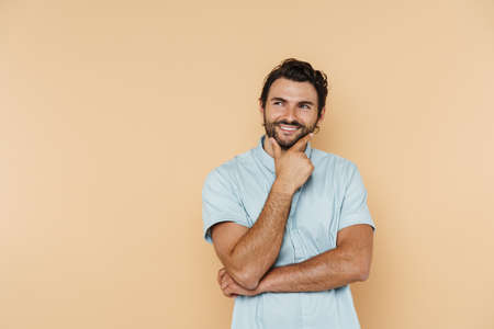 Young white man wearing shirt smiling and looking aside isolated over beige background