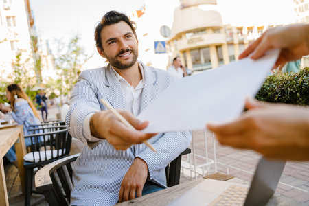 Young man talking with waitress while working with laptop at cafe outdoorsの写真素材