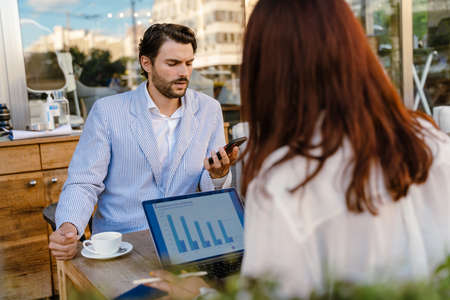 Young man and woman working with gadgets during business meeting at cafe outdoors