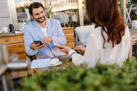 Young man and woman using cellphones during business meeting at cafe outdoorsの写真素材