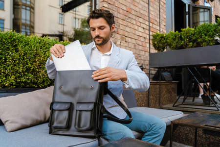 Young man wearing jacket working with laptop while sitting at cafe outdoors