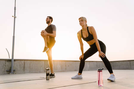 Young man and woman doing exercise while working out together on parking outdoorsの写真素材