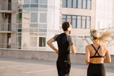Young man and woman in headphones running together on parking outdoors