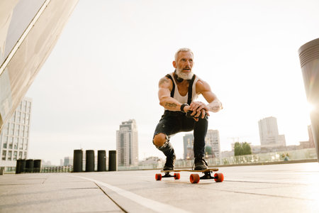 Grey mature man with beard skateboarding on parking outdoorsの写真素材