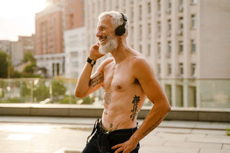 Shirtless mature man listening music with headphones while standing outdoorsの写真素材