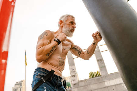 Shirtless mature man with tattoo boxing working out on sports ground outdoorsの写真素材