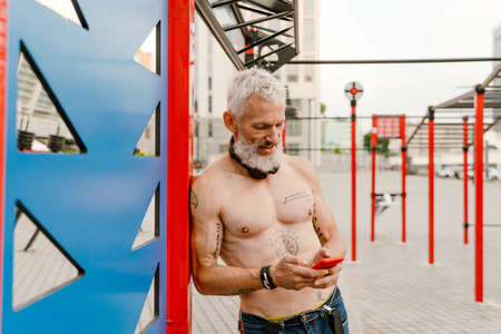 Adult white shirtless man using cellphone while doing workout at sports groundの写真素材