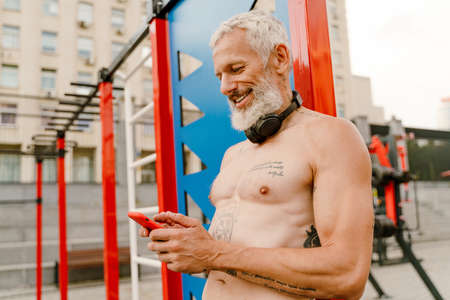Adult white shirtless man using cellphone while doing workout at sports groundの写真素材