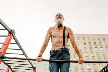 Adult white shirtless man doing workout using horizontal bar outdoorsの写真素材