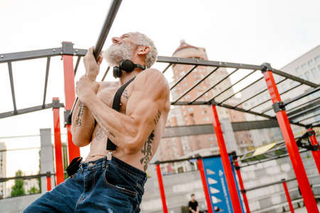 Adult white shirtless man doing workout using horizontal bar outdoors