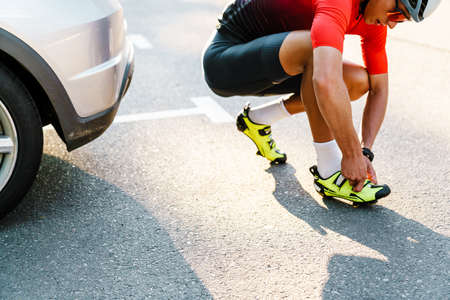 Young white cyclist in helmet wearing shoes while working out at city street