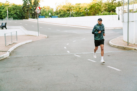 Young sportsman running while working out on city road outdoors