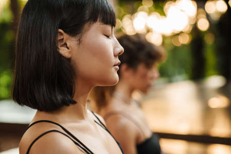 Multiracial two women meditating during yoga practice outdoorsの写真素材