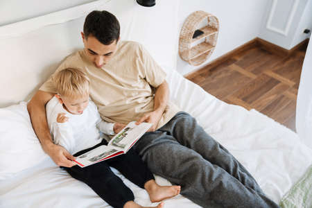 Young white father reading book with his son on bed at homeの写真素材