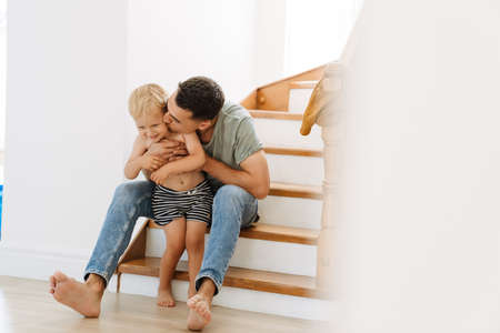 Young white father kissing and hugging his son on stairs at home