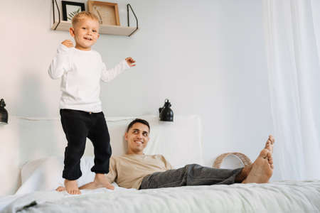 White boy laughing and jumping on bed while spending time with his father at homeの写真素材
